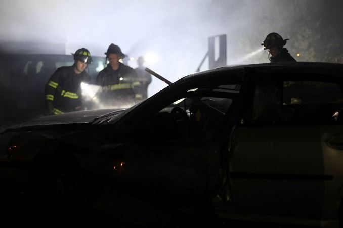Firefighters at night inspecting a car crash